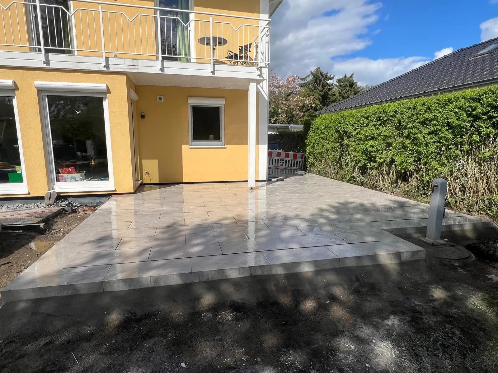 Neu verlegte Terrassenplatten vor der Terrassentür des gelben Hauses, die Umgebung noch unbefestigt.