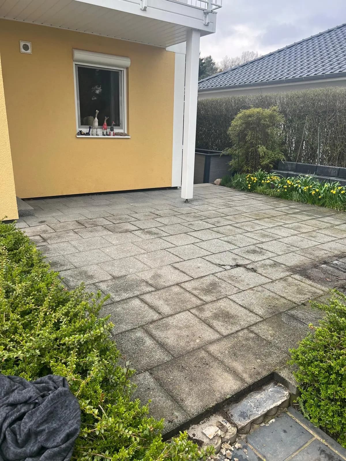 Alte Terrassenfläche aus verwitterten Betonplatten vor dem gelben Haus.